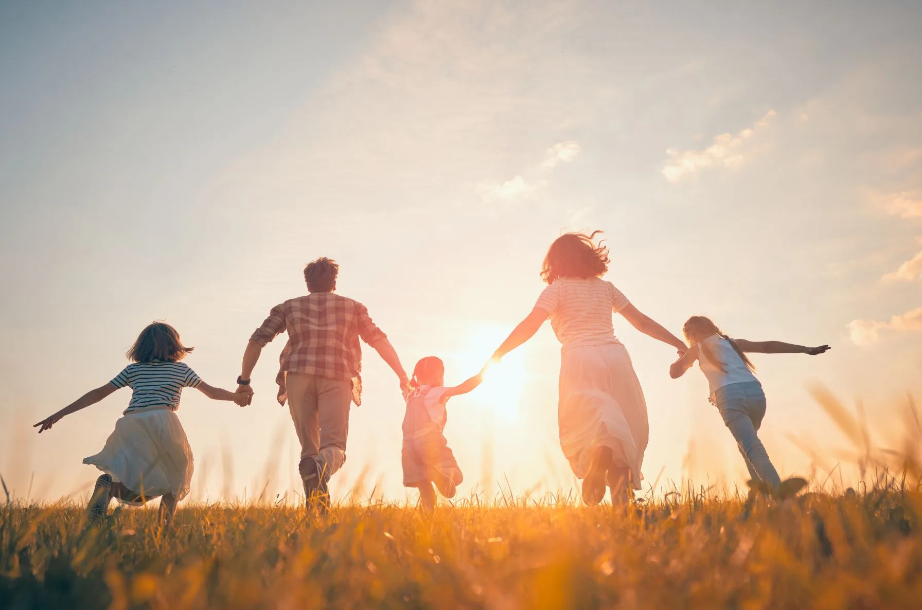 PlusOneTrip large family travel memories - happy parents and children holding hands walking on beach at sunset